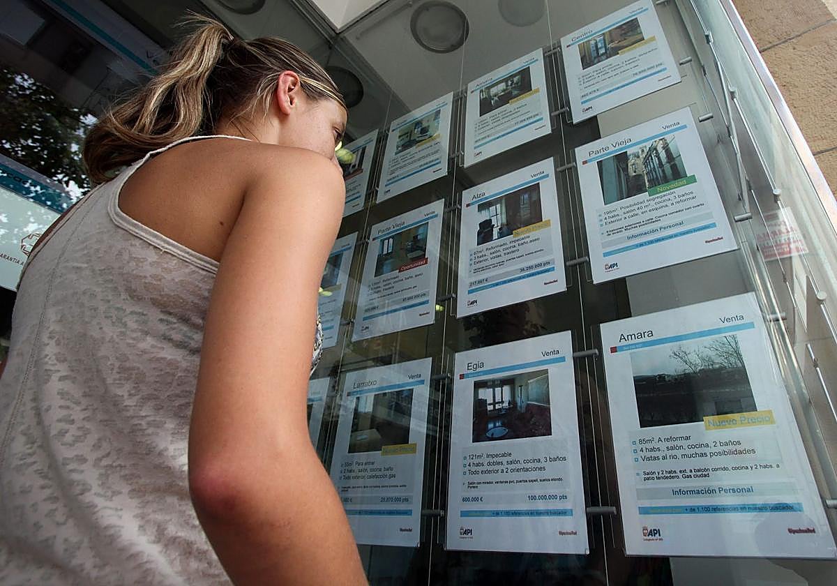 Una joven mira el escaparate de una inmobiliaria.