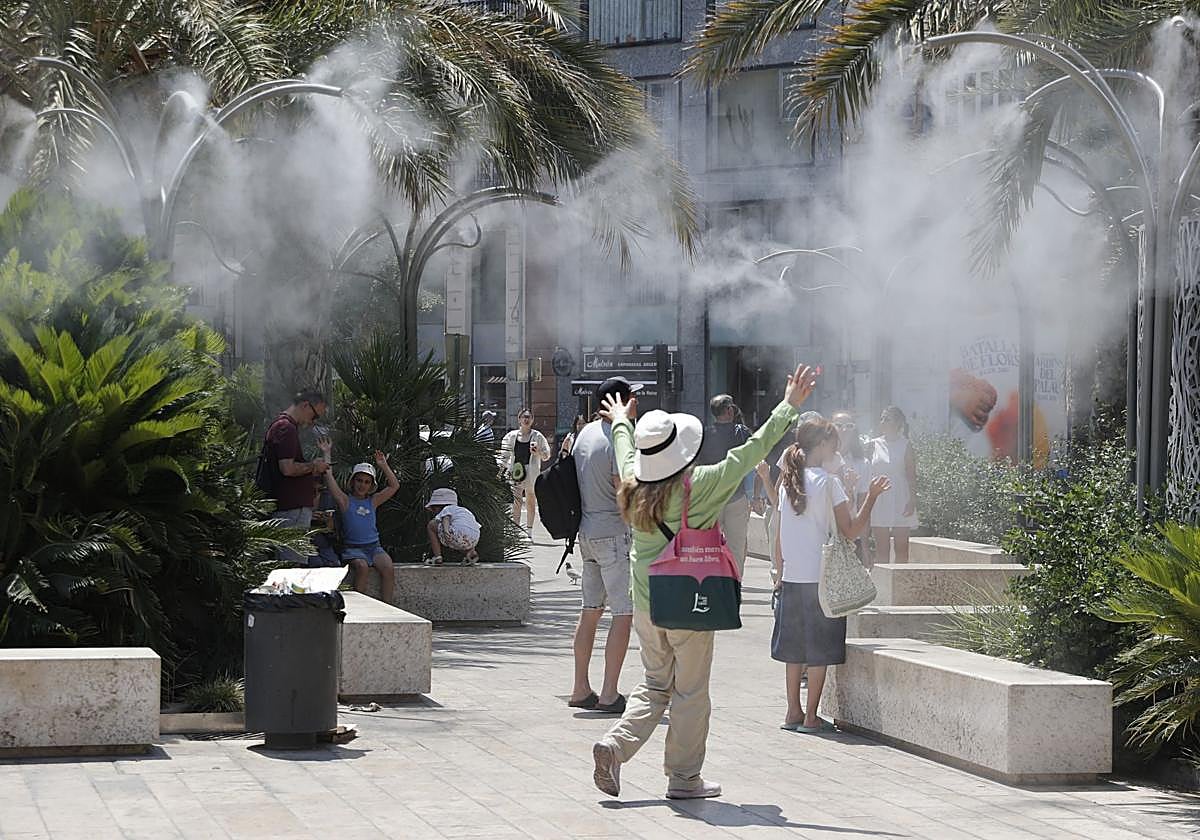 Varios turistas tratan de mitigar el calor bajo una nube de agua vaporizada.