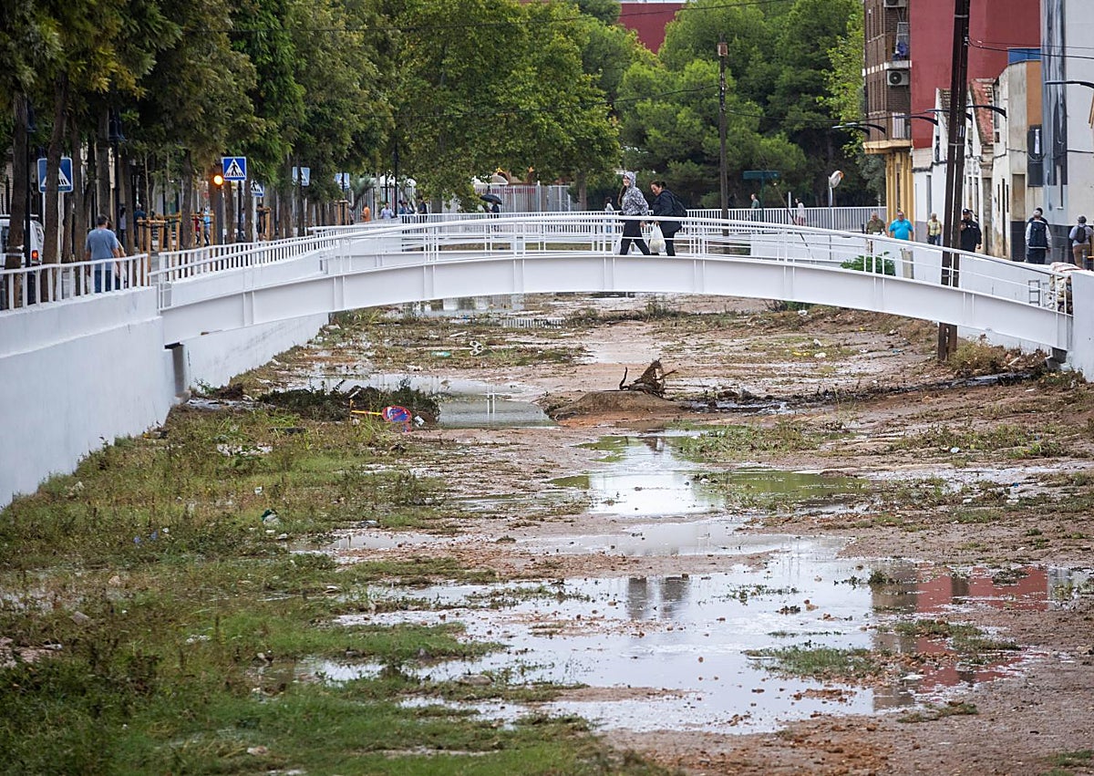 Imagen secundaria 1 - Vehículos estacionados en el puente de Castellar-Oliveral para prevenir que sean arrastrados. Estado del barranco de la Salera a la altura de Aldaia y dos hombres se cubren con chubasqueros en Valencia.