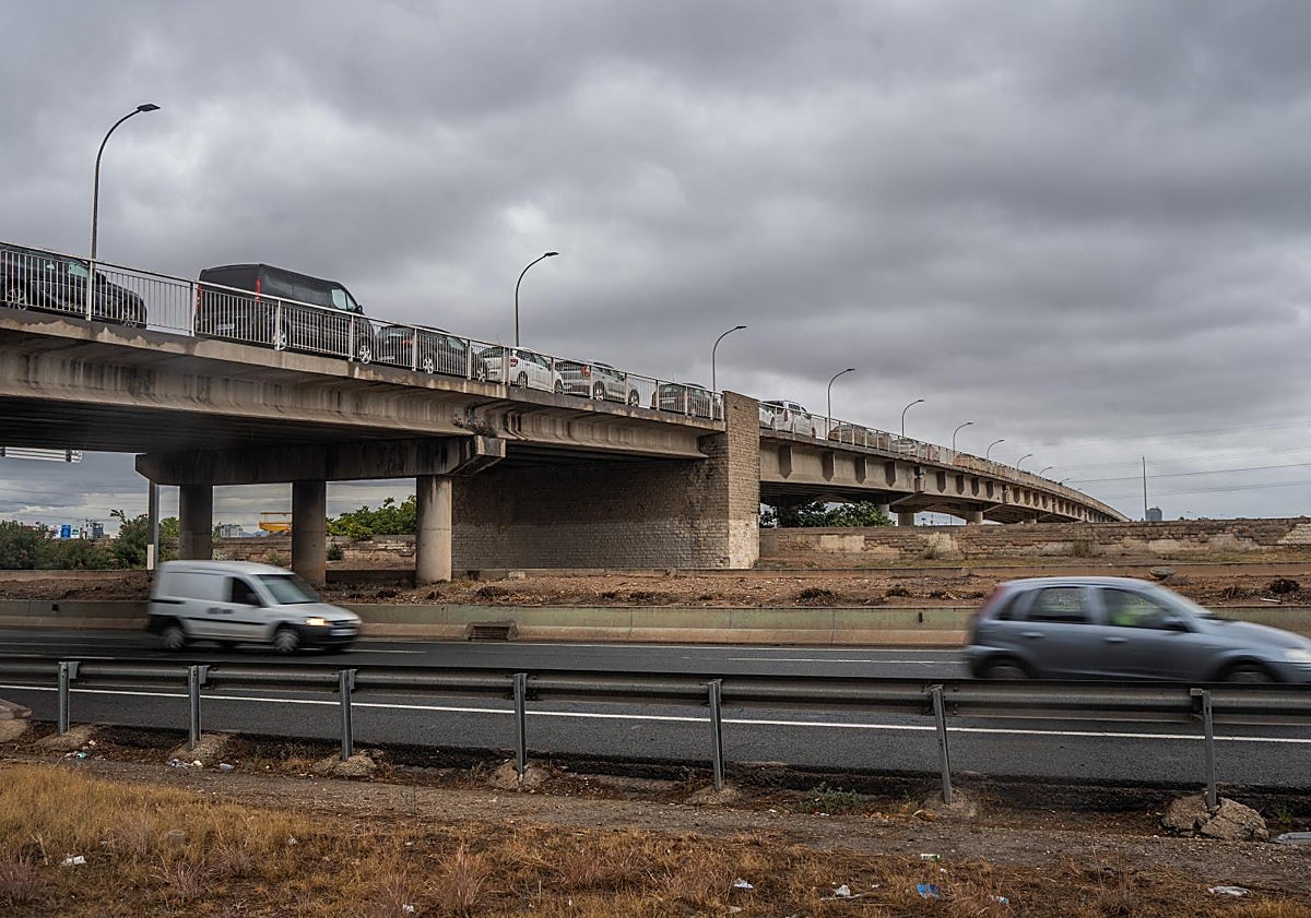Imagen principal - Vehículos estacionados en el puente de Castellar-Oliveral para prevenir que sean arrastrados. Estado del barranco de la Salera a la altura de Aldaia y dos hombres se cubren con chubasqueros en Valencia.