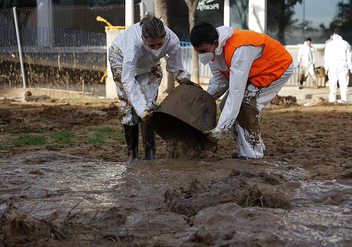 Dos personas depositan lodo sacado de la piscina municipal de Picanya.