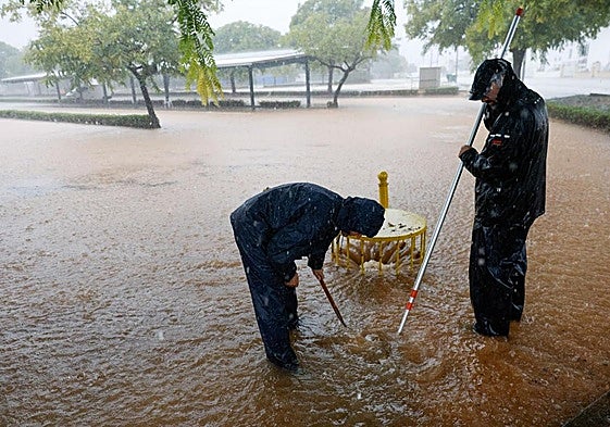 Unos operarios facilitan el drenaje del agua a través de una alcantarilla en Almussafes.