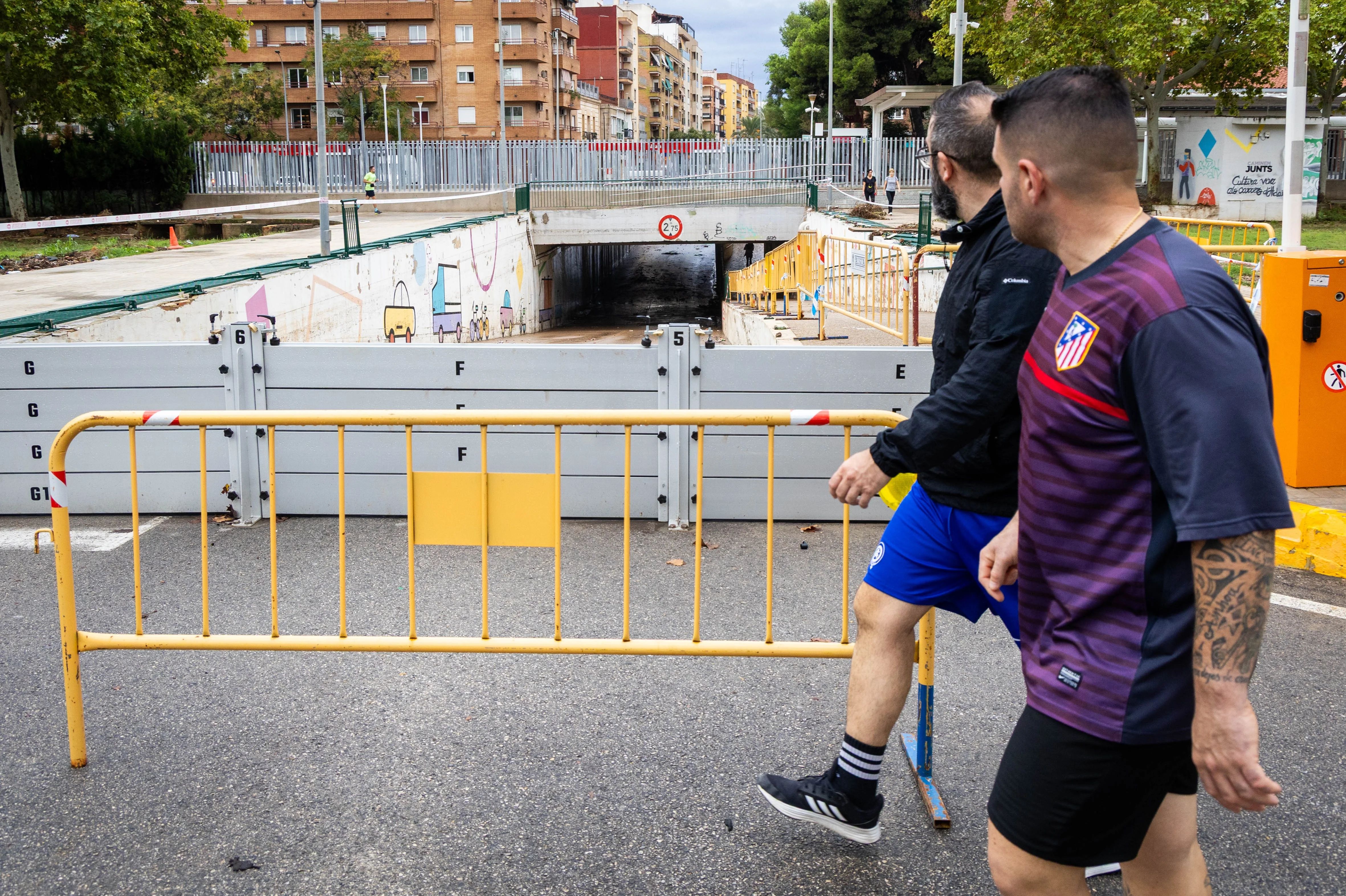 Dos jóvenes pasan este domingo ante un paso inferior inundado en Aldaia.