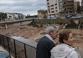 Dos personas observan el barranco de Chiva a su paso por Paiporta, este lunes.