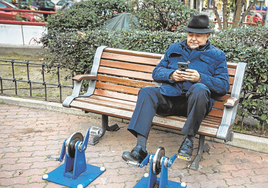 Un jubilado revisa su teléfono sentado en un parque, imagen de archivo.