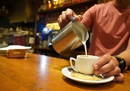 Un camarero pone leche en un café.