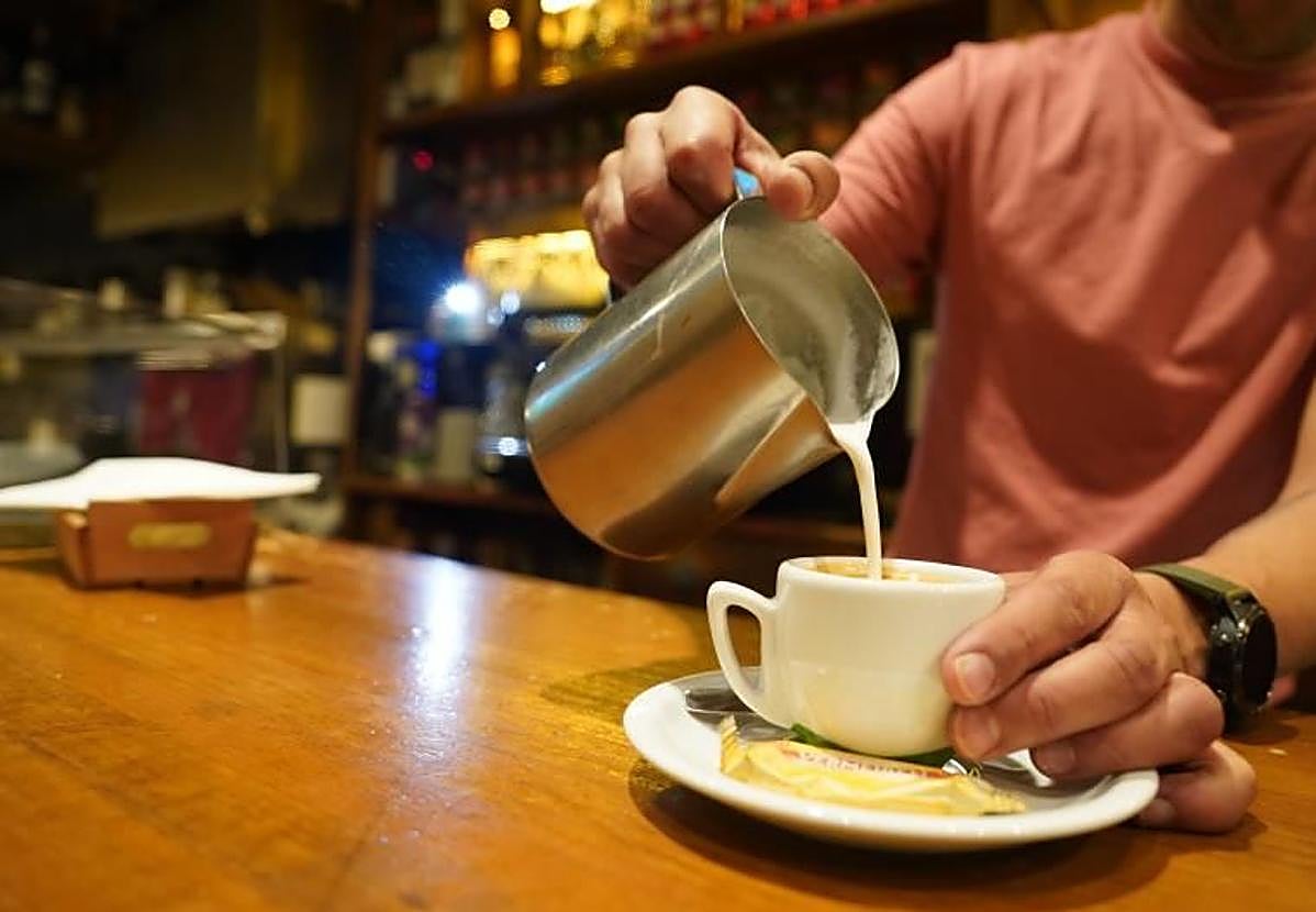 Un camarero pone leche en un café.