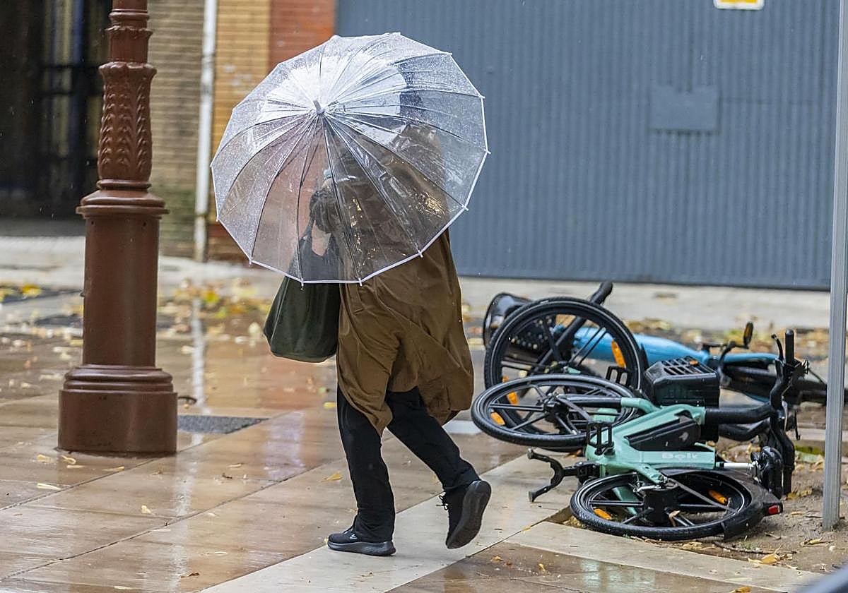 Una mujer con paraguas pasa ante unas bicicletas caídas.