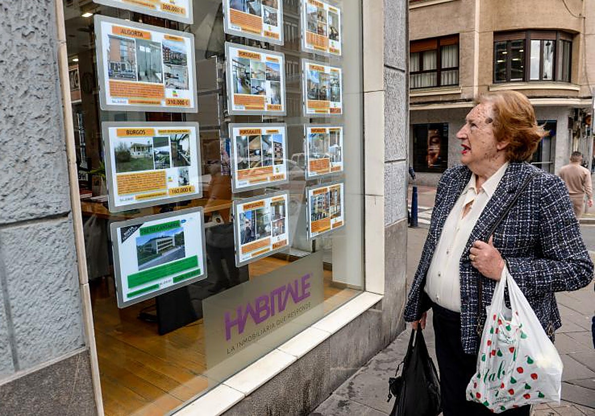 Una mujer observa los inmuebles que ofrece una inmobiliaria en su escaparate