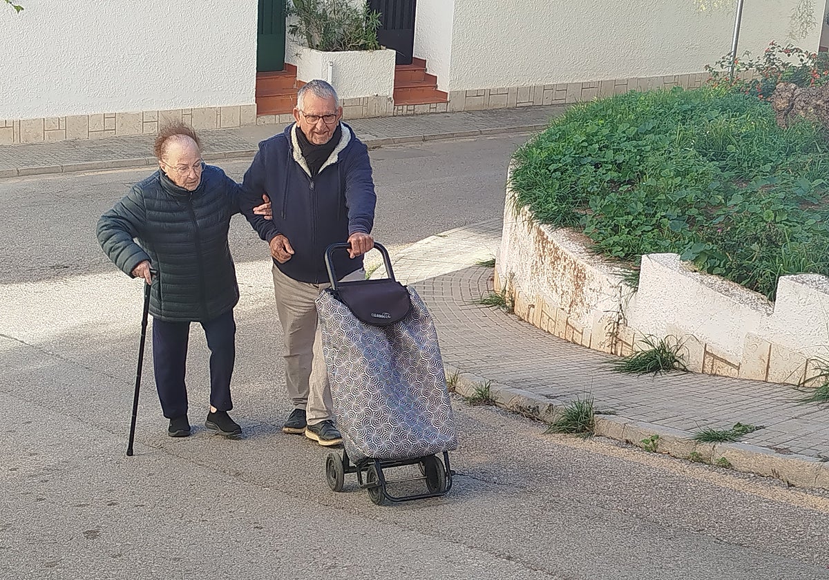 Vicenta se coge al brazo de Antonio, que le ayuda a subir la rampa con el carro de la compra.