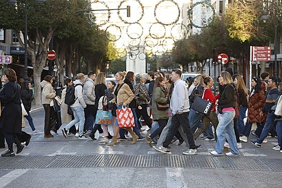 Viandantes con sus compras por un paso de peatones de Valencia en este Black Friday.