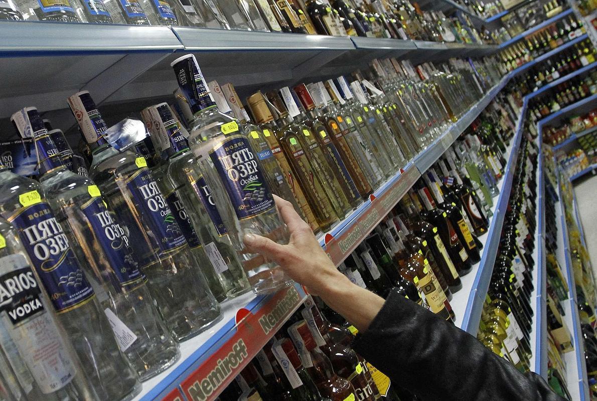 Una mujer coge una botella de vodka de las estanterías de un supermercado. 