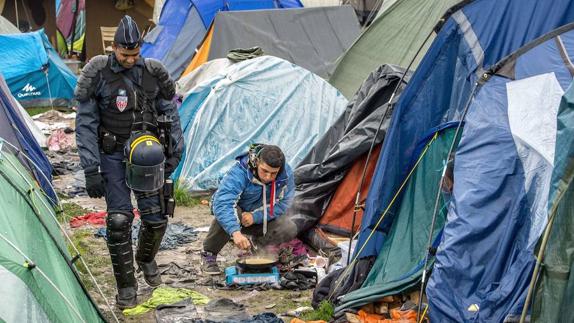 Agente de policía francés andando entre las tiendas de campaña de un campamento de refugiados en Francia.