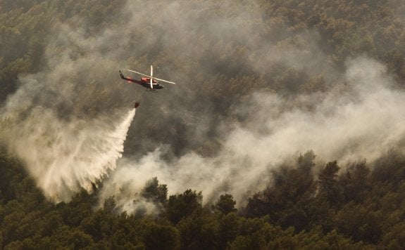 Un helicóptero realiza una descarga de agua en un paraje montañoso afectado por el incendio. :: damián torres