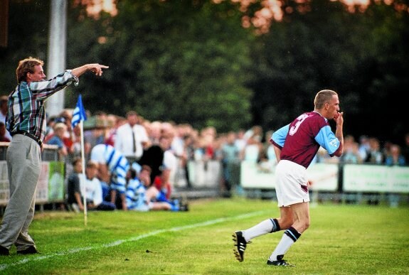 Steve Davies salta al campo del Oxford City con el número 3 del West Ham a la espalda. A la izquierda, el técnico Harry Redknapp realiza indicaciones. 