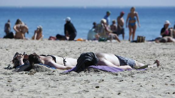 Dos personas toman el sol en la playa del Postiguet de Alicante.