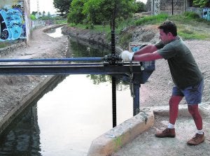 Toni maneja el torno que levanta poco a poco una compuerta en el canal principal,  junto al viejo molino del Batán, en Paterna. / V. Lladró