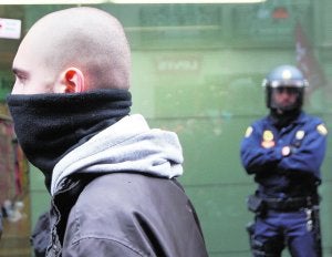 Un joven oculta su rostro mientras un policía controla una protesta en el centro de Valencia. ::                             J.MONZÓ