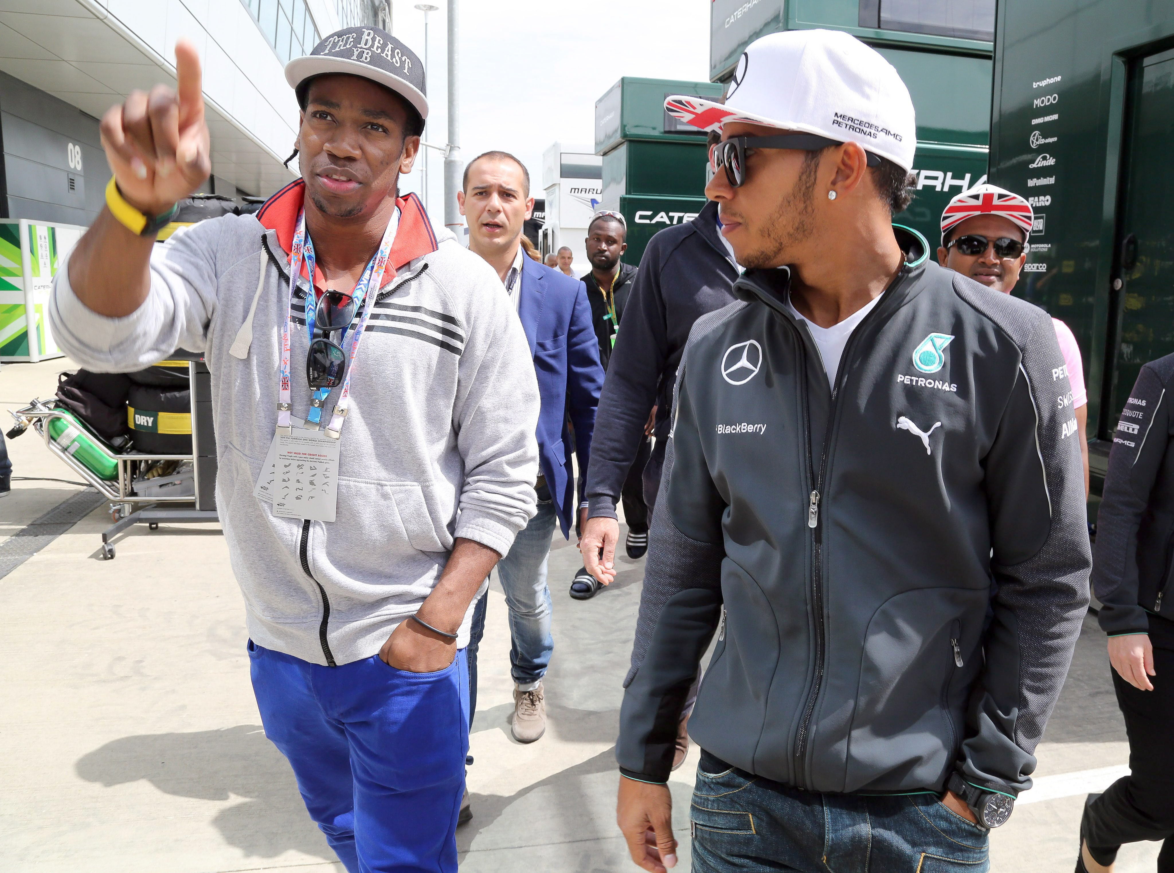 El corredor jamaicano Yohan Blake (i) y el piloto Lewis Hamilton (d) caminan por el paddock de Silverstone.