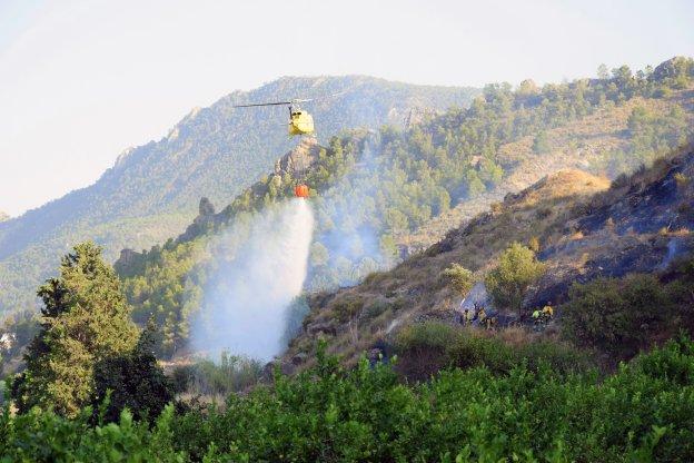 Un helicópero lanza agua y los brigadistas actúan en la ladera.