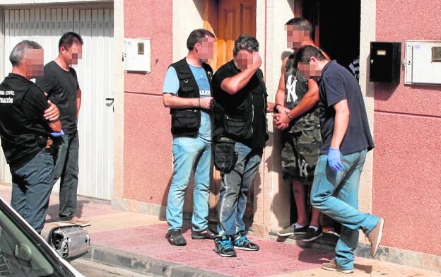 Uno de los detenidos, con las esposas puestas, rodeado de guardias civiles a la puerta de su casa. 