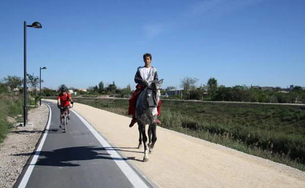 Imagen principal - Un ciclista a punto de adelantar a un jinete, en el tramo del carril-bici que pasa junto a Alcantarilla, un poste señalizador en la contraparada y una señal con indicaciones.