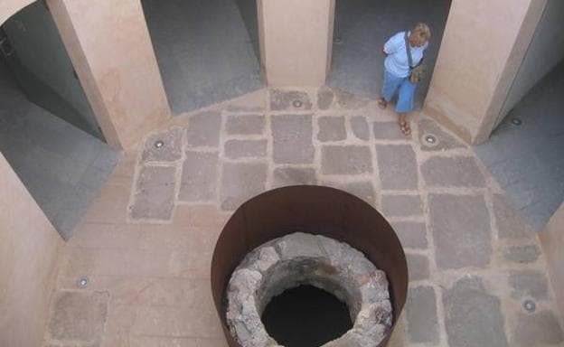 Imagen principal - El patio interior de la fortaleza, con su pozo, una puerta acristalada de la batería de San Pedro y el castillo de Águilas, en lo alto del monte.