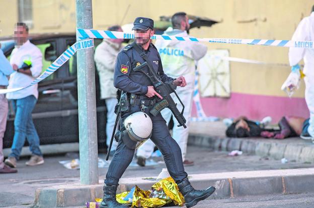 Un agente de la Policía Nacional, con una metralleta, pasa ante la escena del crimen. Al fondo, los dos cadáveres, tendidos sobre la acera.