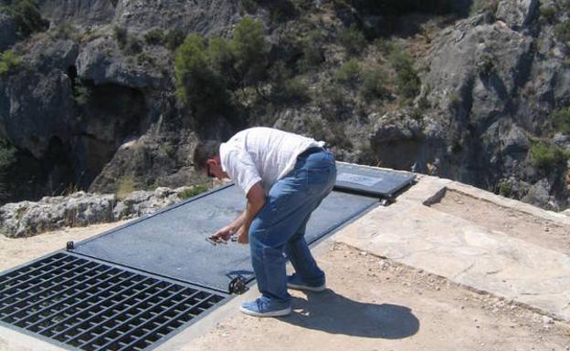 Imagen principal - Un hombre abriendo la entrada a la Cueva de la Serreta, las escaleras de bajada a la misma, y tres visitantes en la terraza volada sobre el cañón.