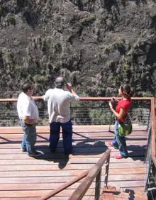 Imagen secundaria 2 - Un hombre abriendo la entrada a la Cueva de la Serreta, las escaleras de bajada a la misma, y tres visitantes en la terraza volada sobre el cañón.