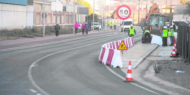 Obreros colocan unas barreras de seguridad en la carretera de Cala Cortina, mientras unos vecinos pasean por la otra acera.
