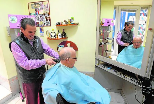 José Carlos García, en su peluquería, le corta el pelo a un cliente.