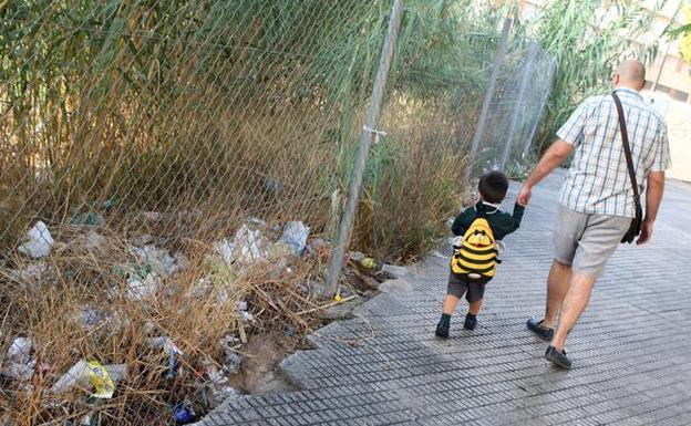 Un padre lleva a su hijo al colegio por un camino repleto de basura en Murcia en una imagen de archivo, 