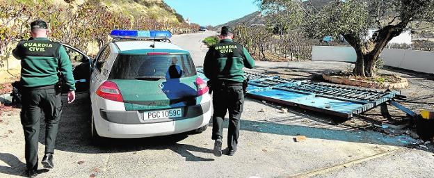 Dos agentes de la Guardia Civil observan la puerta reventada de entrada a la finca.