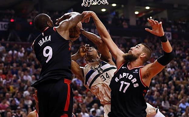 Serge Ibaka (i) y Jonas Valanciunas (d) tratan de frenar una entrada a canasta de Giannis Antetokoumpo.
