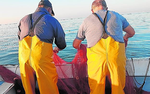 Dos pescadores de San Pedro recogen las redes desde uno de sus barcos.