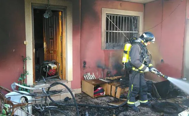 Un bombero sofoca las llamas en el porche de la vivienda incendiada. 