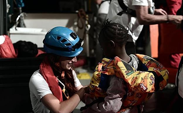Imagen principal - Una cooperante coloca el chaleco salvavidas a un menor a bordo del 'Aquarius' (EP) | La ONG SOS Mediterranee reparte víveres a bordo del buque (AFP).