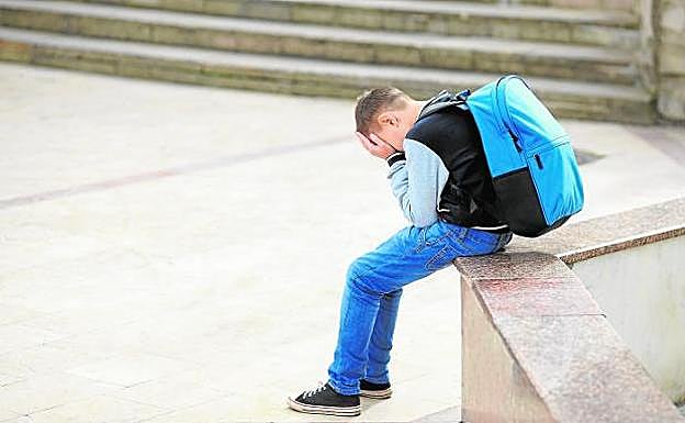 Un escolar sentado en la calle con la cara cubierta. 
