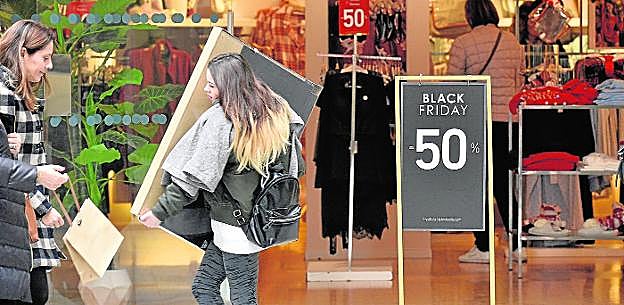 Una mujer carga con un paquete, ayer, junto a un establecimiento comercial con la promoción del 'Black Friday', en pleno centro de Murcia. 