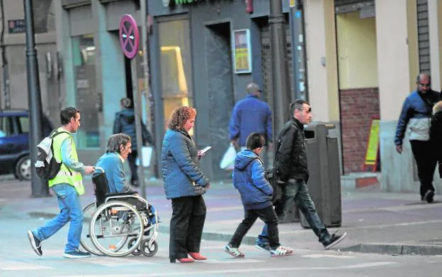 Un hombre empuja una silla de ruedas con un discapacitado para cruzar por un vado. 