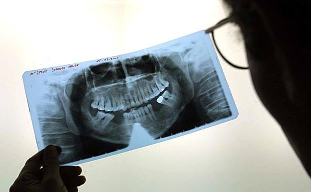 Un dentista examina la radiografía de la boca de un cliente.