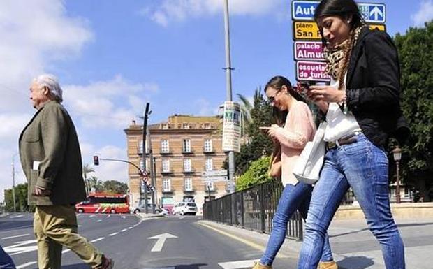 Dos jóvenes cruzan el paso de peatones de Teniente Flomesta sin dejar de mirar sus móviles. 