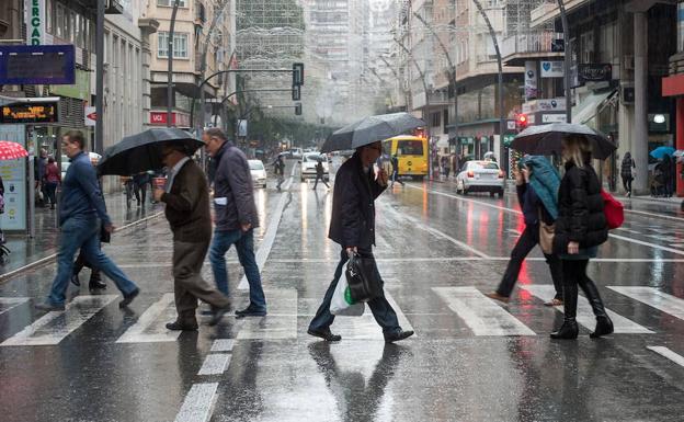 Un grupo de peatones cruza la Gran Vía de Murcia cubiertos por sus paraguas.