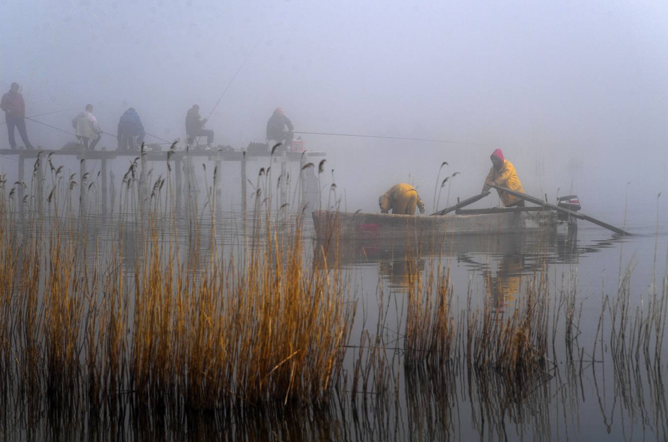 Varias personas pescan bajo la niebla en las orillas del lago Dojran, Macedonia. El lago Dojran es una reserva natural que atrae a diferentes especies de aves debido al clima relativamente cálido y la gran cantidad de peces.