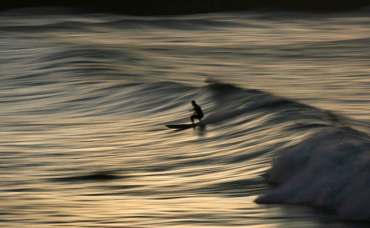 Un surfista coge una ola al atardecer en una playa cerca de Auckland (Nueva Zelanda). 