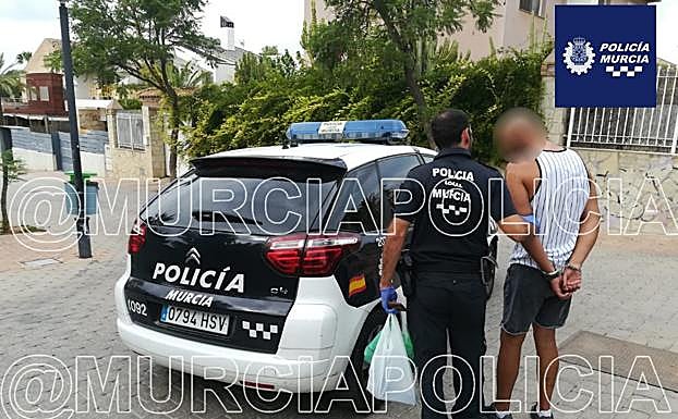Un agente detiene conduce al atracador al coche patrulla.