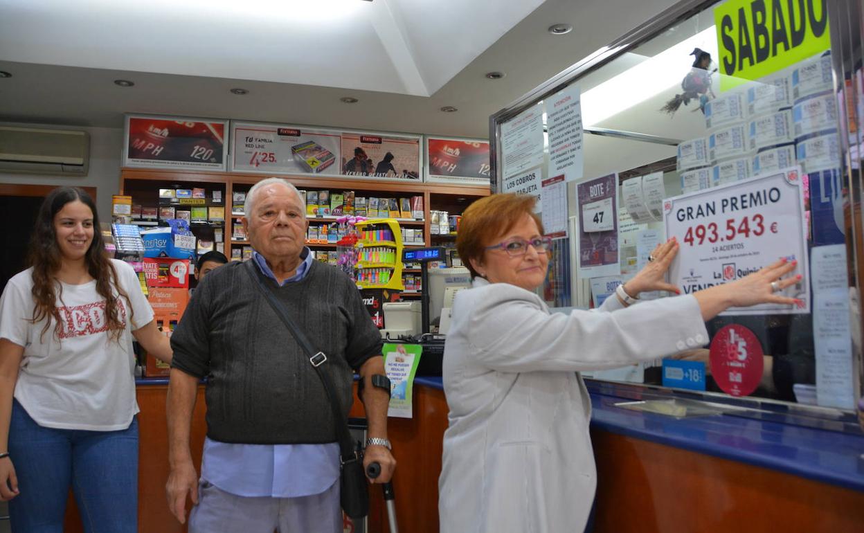 María Fuencisla Lucas (derecha), titular de la administración de loterías que selló la quiniela premiada, colgando el cartel que anuncia el premio.