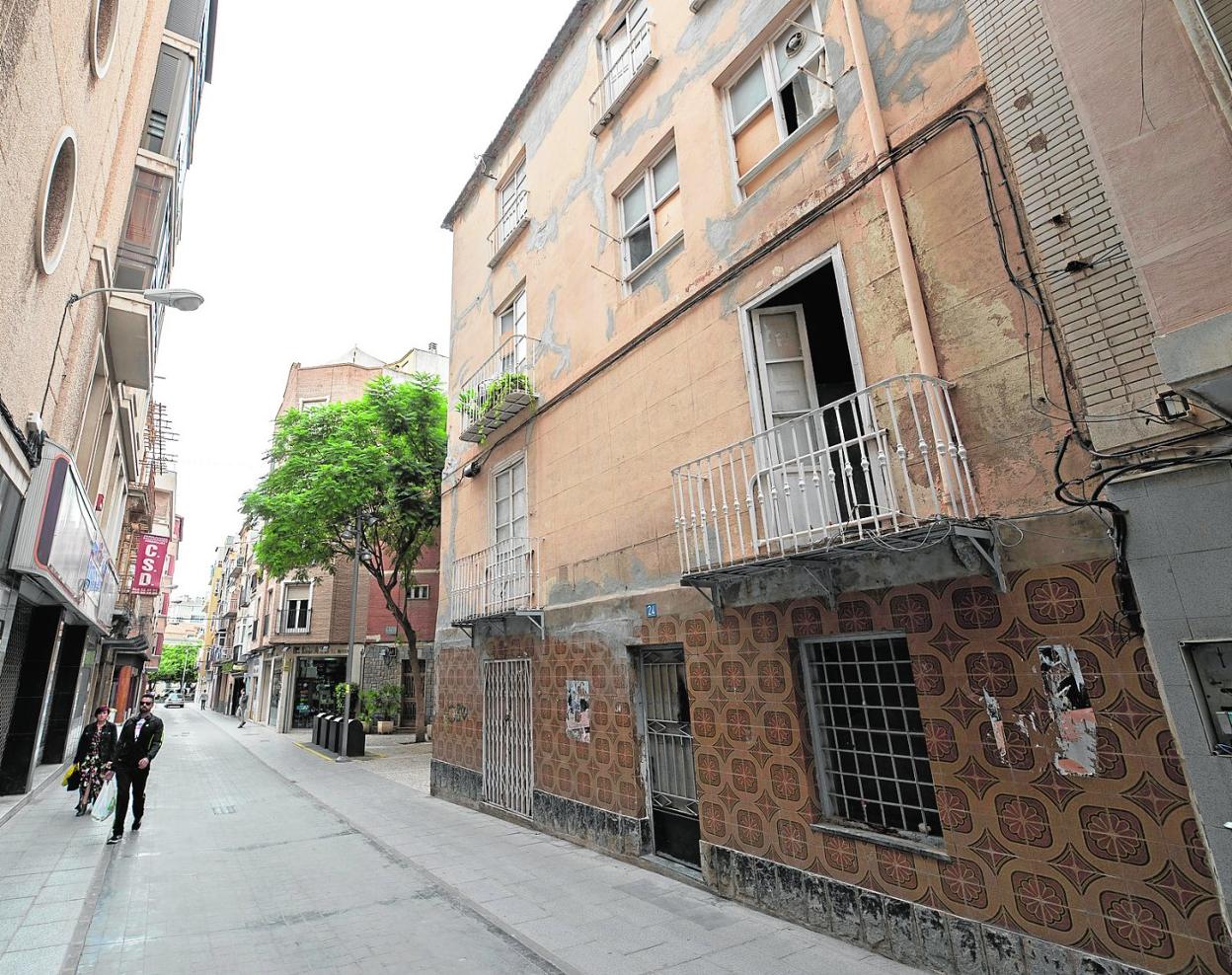 Dos personas caminan frente a un edificio ocupado (a la derecha), en la calle San Vicente, esquina con Plaza del Sevillano. 