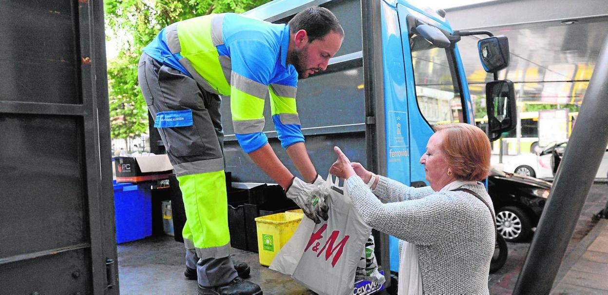 El operario de un punto móvil recoge varias bolsas que recicla una vecina. 